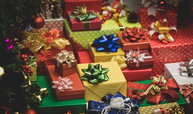 Gros plan d'un grand nombre de coffrets cadeaux emballés pour le réveillon de Noël avec des rubans colorés et des arcs avec décoration de pin de Noël avec des boules de sphère brillantes, des chaussettes, des flocons de glace à proximité.