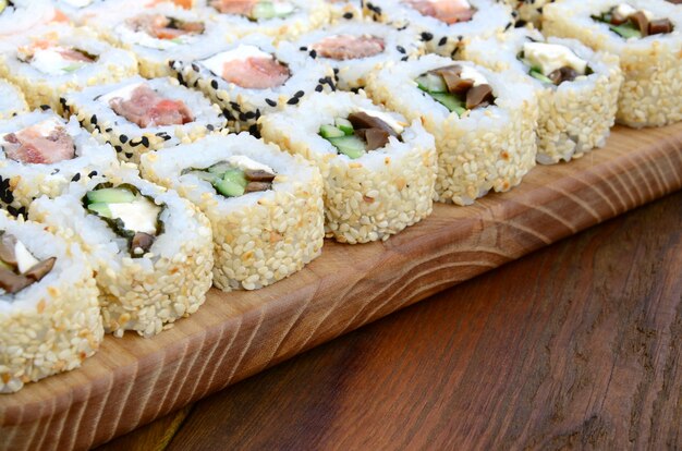 Gros plan d&#39;un grand nombre de rouleaux de sushi avec différentes garnitures se trouvent sur une surface en bois.