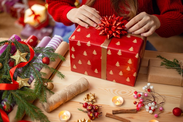 Gros plan d'une grande boîte cadeau enveloppé dans du papier d'emballage festif sur la table fille collant un grand arc dessus les préparatifs des cadeaux de Noël