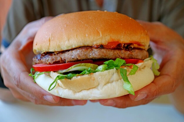 Gros plan sur un gros et savoureux hamburger tenu à la main