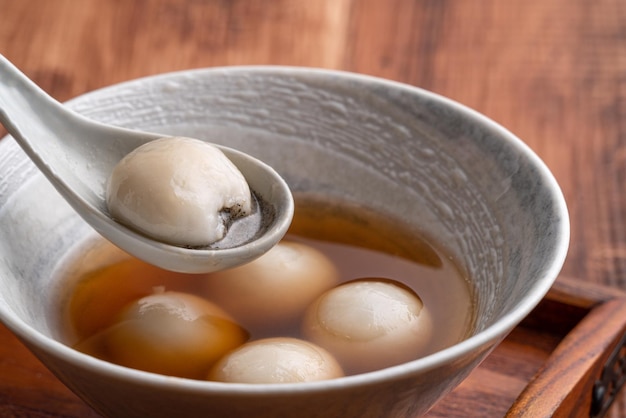 Gros plan sur un gros tangyuan au sésame (tang yuan, boulettes de riz gluant) avec une soupe au sirop sucré dans un bol sur fond de table en bois pour la nourriture du festival du solstice d'hiver.