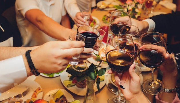 Gros plan d'un groupe de personnes tintant des verres avec du vin ou du champagne devant l'arrière-plan de bokeh. les mains des personnes âgées.