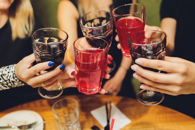 Gros plan d'un groupe de personnes tinter les verres avec du vin ou du champagne en face de bokeh