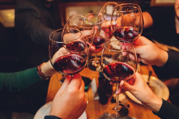 Gros plan d'un groupe de personnes tinter les verres avec du vin ou du champagne en face de bokeh