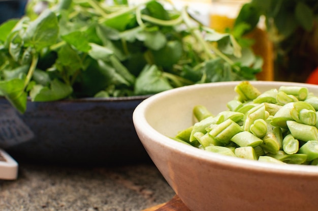 Gros plan de haricots verts hachés dans un bol en céramique blanche avec de la salade en arrière-plan sur un comptoir de cuisine en granit