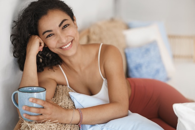 Gros plan heureux jeune femme en bonne santé avec des cheveux bouclés sombres couché dans un canapé confortable dans une terrasse