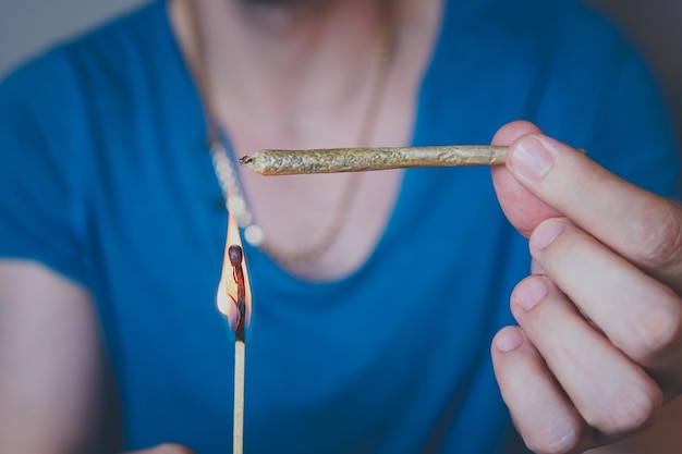 Gros plan d'un homme adulte s'allume avec des allumettes et fume un joint de marijuana médicale