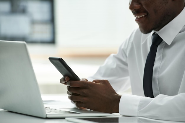 Gros plan d'un homme d'affaires afro-américain utilisant un smartphone et souriant assis à table devant