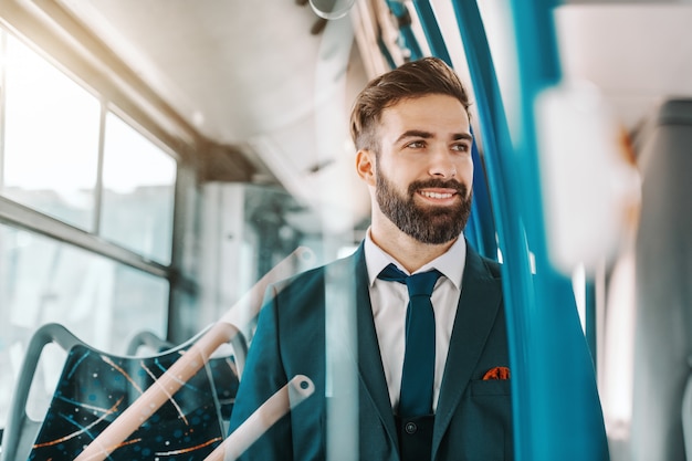 Gros Plan D'un Homme D'affaires Barbu Souriant En Tenue De Soirée Assis Dans Les Transports En Commun Et Regardant Par La Fenêtre.