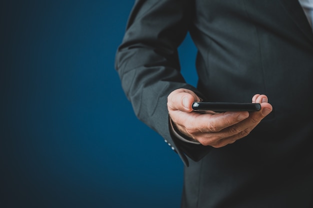 Gros plan d'homme d'affaires dans un costume tenant un téléphone intelligent dans sa main. Sur fond bleu marine.