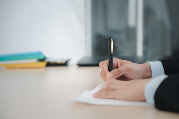 Gros plan de l'homme d'affaires écrivant ou signant un contrat sur papier au bureau.