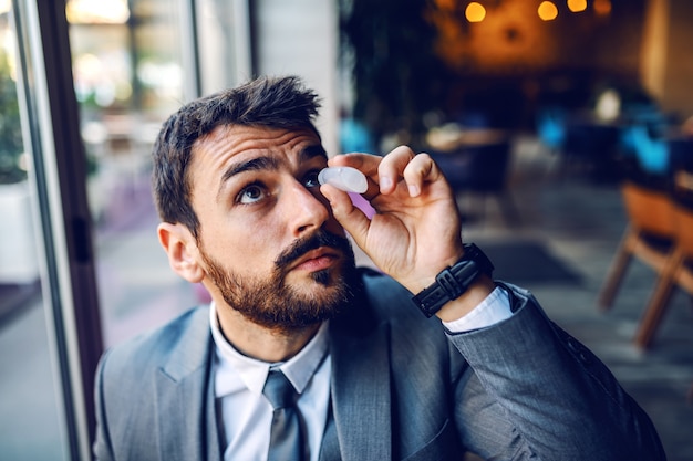 Gros plan d'un homme d'affaires élégant caucasien beau en costume assis dans un café et mettre des gouttes pour les yeux dans les yeux.