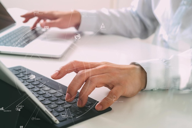 Gros plan d'un homme d'affaires tapant au clavier avec un ordinateur portable et une tablette numérique sur un bureau blanc