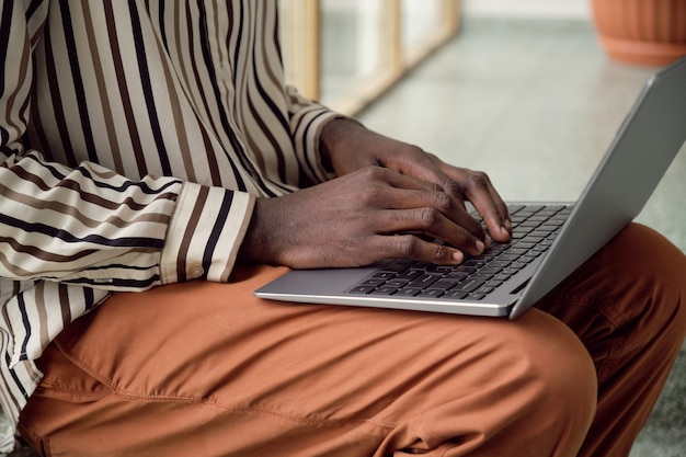 Gros plan d'un homme africain en train de taper sur un ordinateur portable alors qu'il était assis au bureau