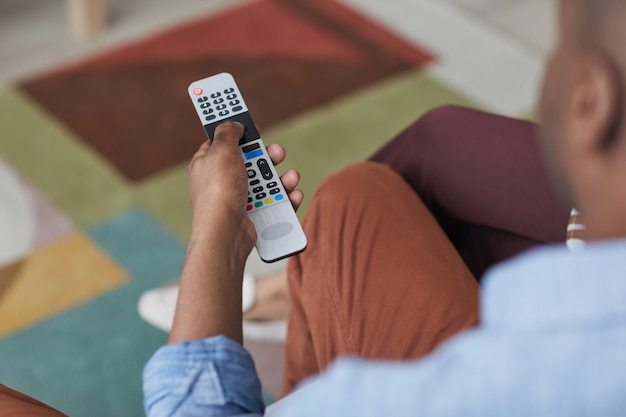 Gros plan d'un homme afro-américain tenant une télécommande de télévision et changeant de chaîne, espace de copie