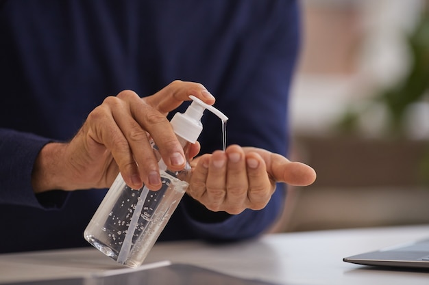 Photo gros plan d'un homme d'âge mûr méconnaissable à l'aide d'un désinfectant pour les mains tout en se lavant les mains sur le lieu de travail, copiez l'espace