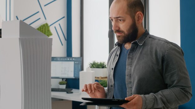 Photo gros plan sur un homme architecte utilisant une tablette numérique pour concevoir un modèle de bâtiment et un agencement au bureau. entrepreneur expert travaillant avec un appareil pour planifier un projet de construction et une structure urbaine.