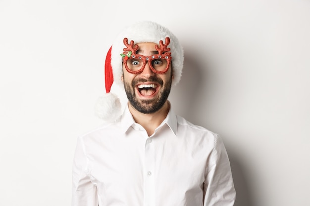 Gros plan d'un homme barbu excité dans des verres de Noël et bonnet de Noel à la surprise de l'offre promo, concept de publicité de vacances d'hiver, fond blanc.