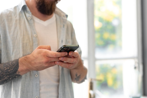 Gros plan d'un homme barbu utilisant un smartphone à la maison