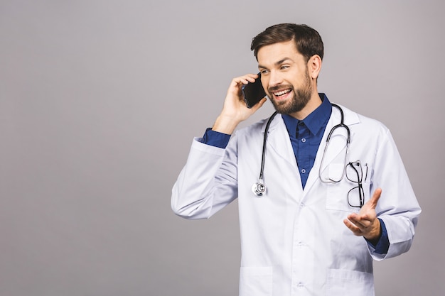 Gros plan d'un homme beau médecin isolé sur fond gris, parler sur smartphone, souriant positivement