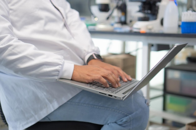 Gros plan de l'homme en blouse de laboratoire à l'aide d'un ordinateur portable en laboratoire