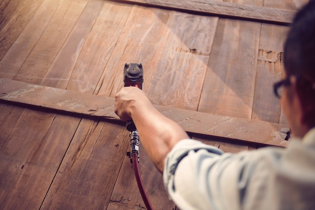 Gros plan d'un homme charpentier à l'aide d'un pistolet à clous.Carpenter à l'aide d'un pistolet à clous pneumatique faisant des travaux de meubles en bois, style vintage