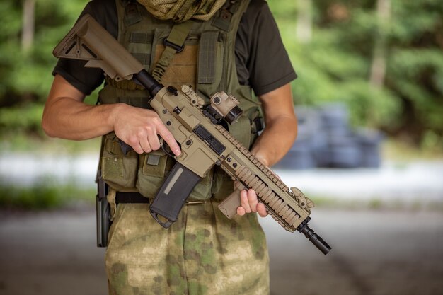 Gros plan d'un homme debout avec un fusil d'assaut airsoft en uniforme militaire