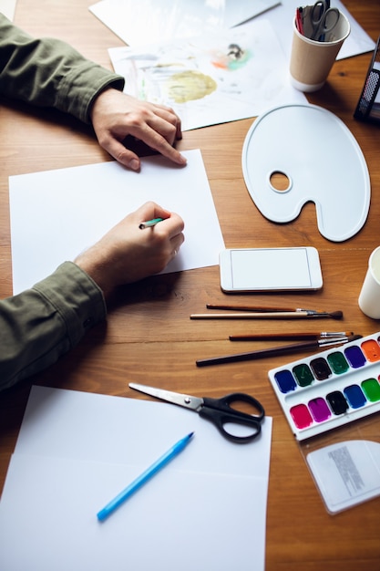 Photo gros plan de l'homme dessin avec des peintures et des crayons à la maison. ambiance confortable. enseignement à distance, occupation créative, art-thérapie. numérisation, utilisation de différents appareils, gadgets. espace de copie.