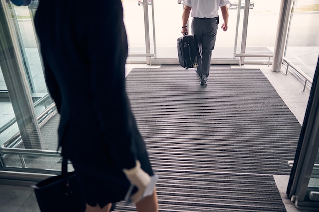 Gros plan sur un homme élégant tenant une valise de voyage et se dirigeant vers la porte de sortie tandis qu'une femme d'affaires se tenait derrière lui