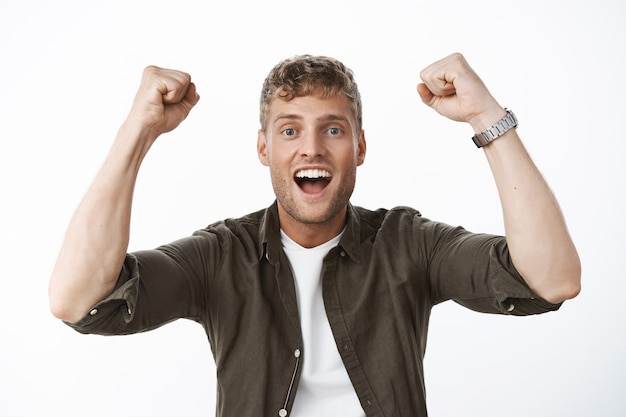 Gros Plan D'un Homme Européen Heureux, Excité Et Ravi, Levant Les Poings En Signe De Triomphe Et De Célébration, Criant Ouais Joyeusement Comme Ayant L'air Plein D'espoir Et Ravi à L'avant Posant Contre Un Mur Gris