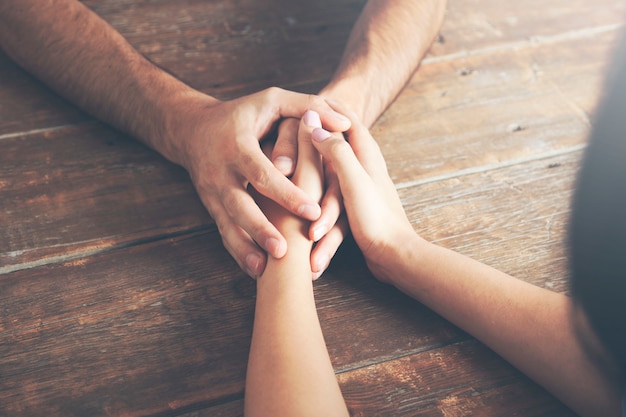 Gros plan sur un homme et une femme se tenant la main à une table en bois