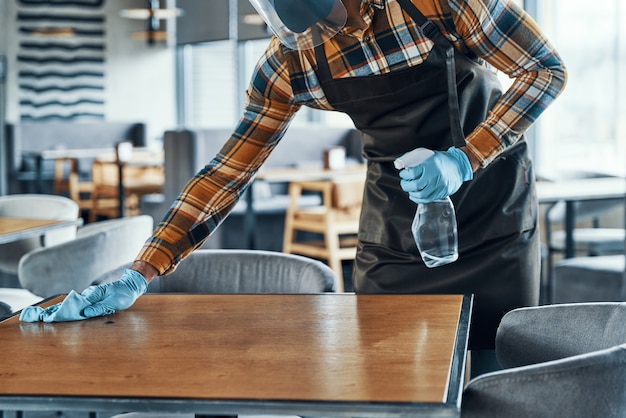 Gros plan de l'homme en gants de protection table de nettoyage au restaurant