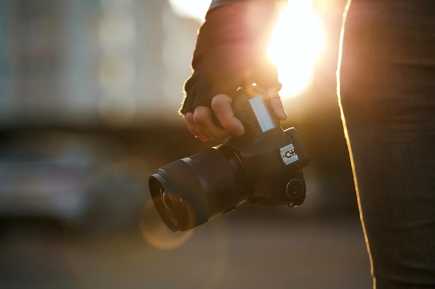 Gros plan d'un homme en gants tenant un appareil photo numérique contre la lumière du soleil. Espace de copie