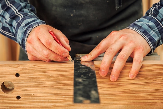 Gros plan L'homme mesure une planche de bois avec une règle et marque au crayon les points nécessaires pour les tranches