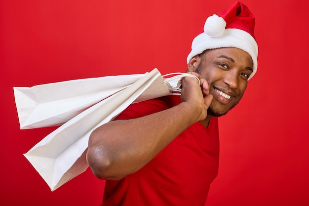 Gros plan d'un homme noir dans un bonnet de Noel qui porte un sac en papier blanc sur le dos comme un sac