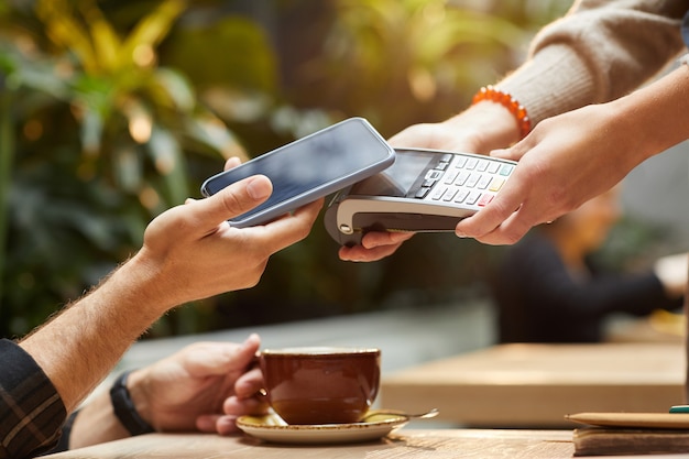 Gros plan d'un homme payant en ligne avec un téléphone mobile pour sa commande au café