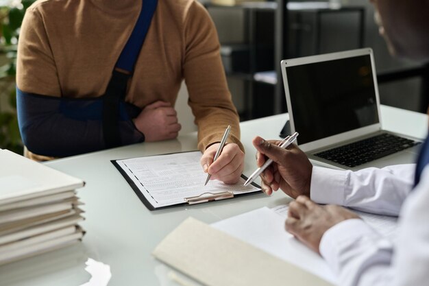 Gros plan de l'homme remplissant le formulaire d'assurance médicale main blessée en écharpe dans l'espace de copie d'arrière-plan