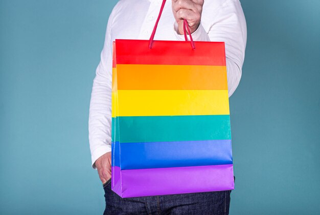 Gros plan de l'homme avec un sac dans les couleurs lgtb sur fond bleu.