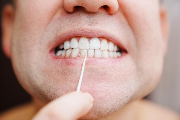 Gros plan un homme se brosser les dents cure-dent en plastique avec du fil dentaire