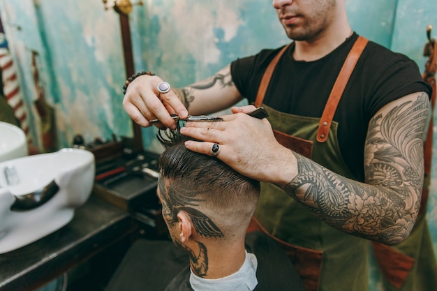 Gros plan d'un homme se faisant couper les cheveux à la mode au salon de coiffure. Le coiffeur masculin en tatouages au service du client.