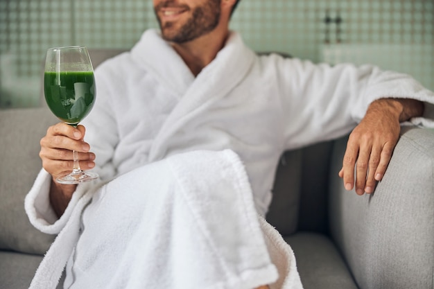 Gros plan d'un homme souriant en peignoir tenant un verre de jus de légumes frais