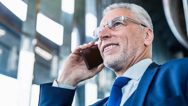 Gros plan d'un homme souriant senior faisant un appel téléphonique au bureau