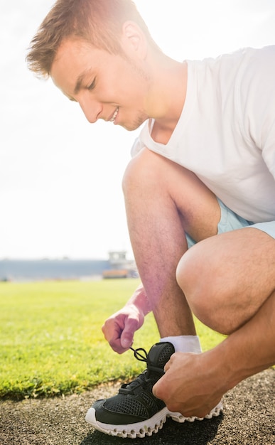 Gros plan d'un homme sportif assis sur la route et nouer des lacets.