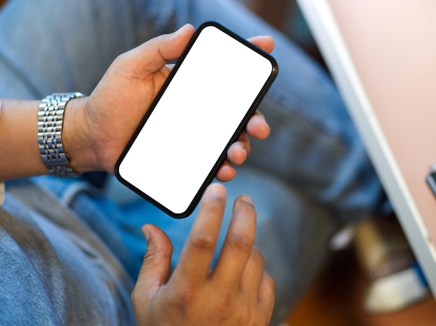 Gros plan sur un homme utilisant son téléphone mobile intelligent assis à sa maquette d'écran vierge de téléphone de bureau