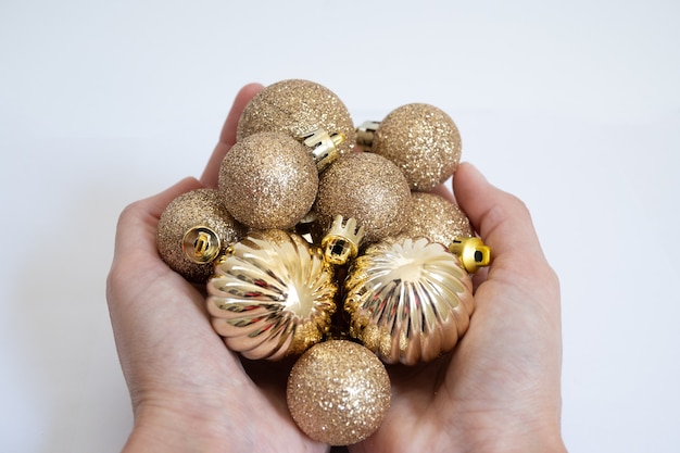 Gros plan horizontal de mains tenant une poignée de boules de Noël dorées, avec un fond blanc.