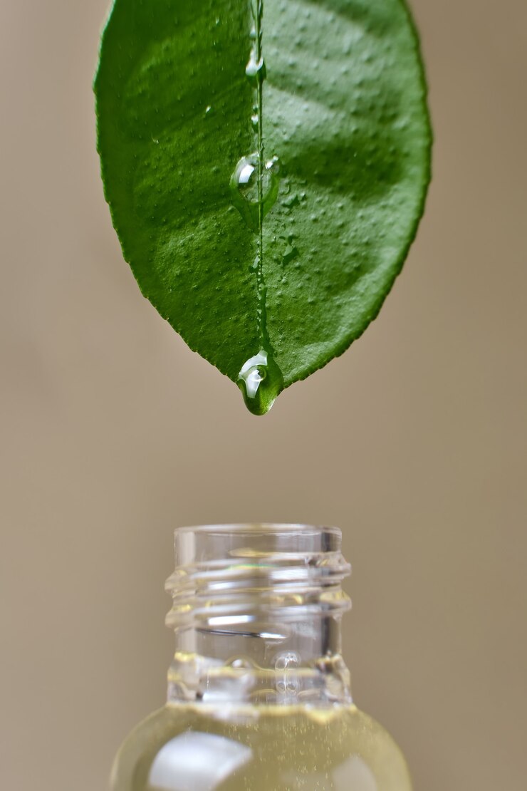 Photo gros plan d'huile essentielle dégoulinant de feuille naturelle fraîche dans une bouteille en verre sur fond beige
