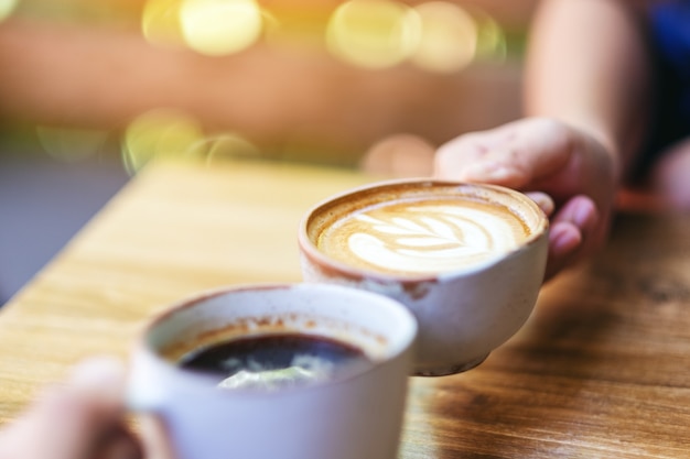 Gros plan image de deux personnes tinter des tasses à café sur une table en bois