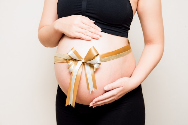 Gros plan image du ventre de femme enceinte avec ruban d'or. Une mère attend le bébé.