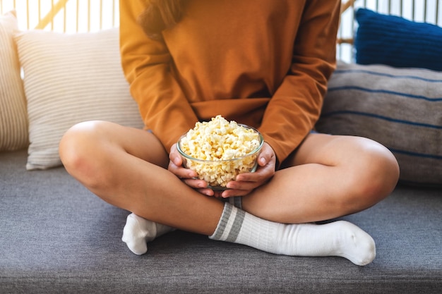 Gros plan image d'une femme tenant un bol de pop corn assis sur un canapé à la maison