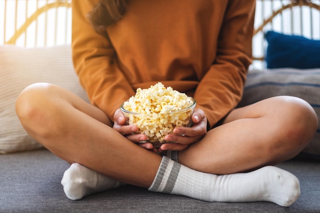 Gros plan image d'une femme tenant un bol de pop corn assis sur un canapé à la maison